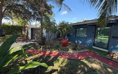 a blue house with a palm tree in the yard at Garden of Manors - Men Only Clothing Optional Boutique Guesthouse in Florida in Fort Lauderdale