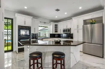 a kitchen with white cabinets and a large island with bar stools at Villa Asher - Waterfront with dock in Miami
