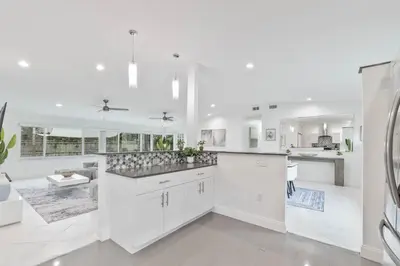 a white kitchen with white cabinets and a large island at Casa Moderna 3 Bed 2 Bath with Private Patio and BBQ in North Miami Beach