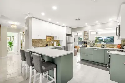 an open kitchen with white cabinets and bar stools at Backyard Oasis 3 Hole Golf Pool Fire Pit in Fort Lauderdale