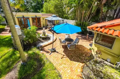 a patio with a blue umbrella and a table and chairs at Walk to Las Olas! Old Florida Oasis with Hot Tub in Fort Lauderdale