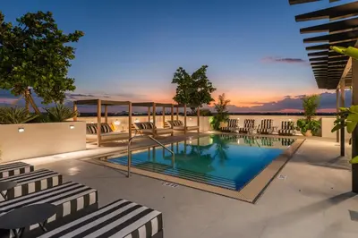 a swimming pool with chairs and a sunset in the background at The Avenue Hotel Coral Gables in Miami