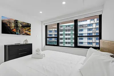 a bedroom with a white bed with two large windows at Stylish 3BR Retreat Steps from the Beach with Resort Amenities 1508 in Miami Beach