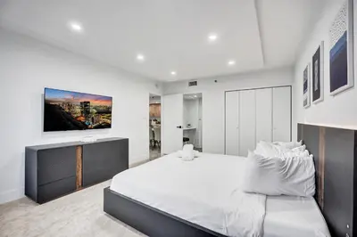 a white bedroom with a large bed and a tv at Modern 3BR Ocean view Condo with Pools, Gym and Sauna 1407 in Miami Beach
