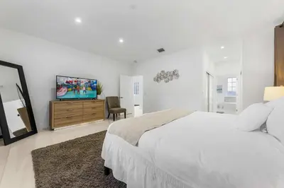 a white bedroom with a bed and a flat screen tv at Renovated house w private heated pool grill in Hollywood