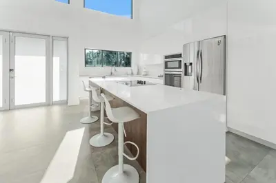 a white kitchen with a large island with stools at Villa Coral Bay in Miami Beach