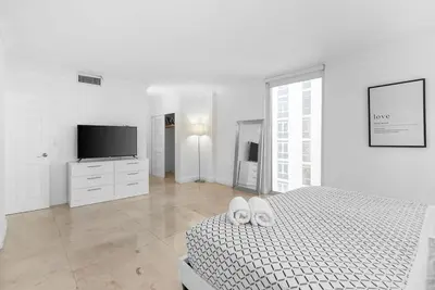 a white bedroom with a bed and a flat screen tv at Oceanfront corner unit in Hollywood