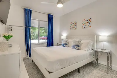 a bedroom with a bed with blue curtains and a window at Walk to Dining and Nightlife! Chic Apt Near Las Olas in Fort Lauderdale