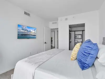a white bedroom with a large bed with a blue pillow at X Lounge VIII-Prime Corner Residence in Miami