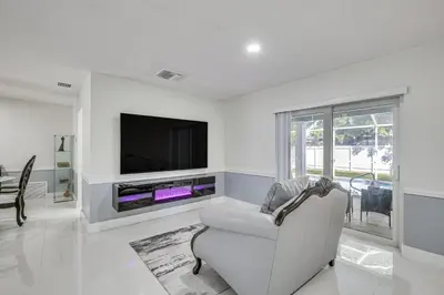 a white living room with a tv and a chair at 3 Mi to Hard Rock Stadium Home with Fenced-In Yard! in Miramar