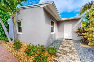 a white house with a palm tree and a driveway at The Front House & Cottage in Fort Lauderdale