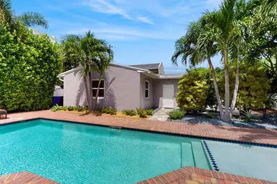 a swimming pool in front of a house with palm trees at The Cottage in Fort Lauderdale