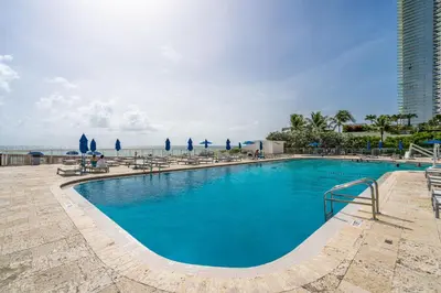 a swimming pool with chairs and the ocean in the background at Beachfront Resort Studio with 2 Queen beds, Balcony & Pool in Sunny Isles Beach