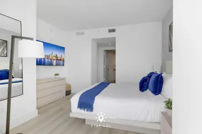 a white bedroom with a large bed with blue pillows at Oceanline 3BR Corner Balcony & Calm Seas in Hollywood