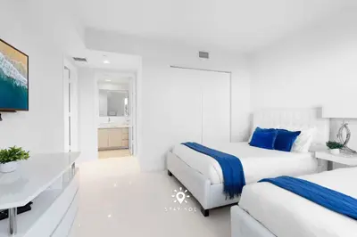 two beds in a white room with a desk and a bedroom at Apt with Private Balcony - Incredible Pool in Hallandale Beach
