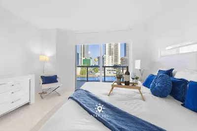 a white bedroom with a large bed and a chair at Apt with Private Balcony - Incredible Pool in Hallandale Beach