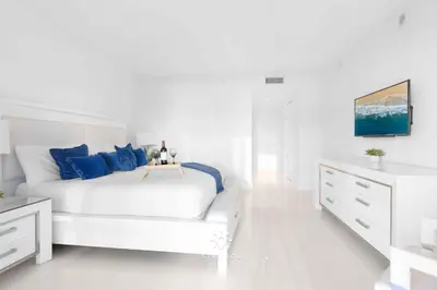 a white bedroom with a bed and a dresser at Apt with Private Balcony - Incredible Pool in Hallandale Beach