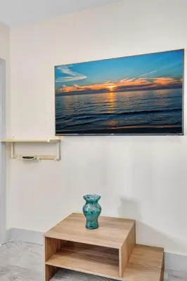 a television hanging on a wall with a vase on a table at Santorini Blu Elegant 1BR Beach Retreat On the Beach in Hollywood