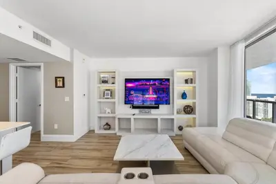 a living room with a white couch and a tv at Luxury Oceanview Condo with Private Foyer at Beachwalk Resort in Hallandale Beach