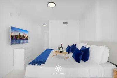a white bedroom with blue pillows and a bed at Luxury Coastal Escape Balcony views - Free Parking in Miami Beach
