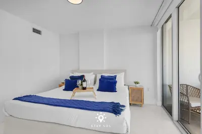 a white bedroom with a large bed with blue pillows at Luxury Coastal Escape Balcony views - Free Parking in Miami Beach
