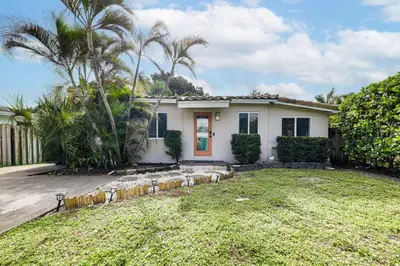 a white house with palm trees and a yard at 5 Mi to Las Olas Beach! Bright Home with Fenced Yard in Fort Lauderdale