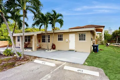 a small yellow house with palm trees and a driveway at The Palms A in Fort Lauderdale