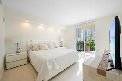 a white bedroom with a bed and a television at Spacious 3BR Condo Across from Beach with Ocean & City Views in Sunny Isles Beach