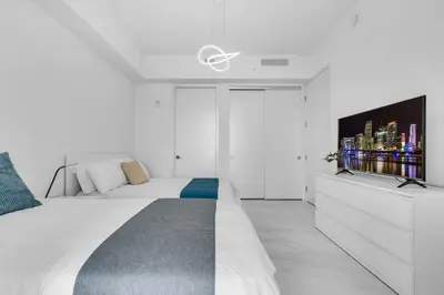 a white bedroom with a bed and a tv on a dresser at Chic OceanView 2 Bedroom with Free Parking Pool Jacuzzi in Sunny Isles Beach