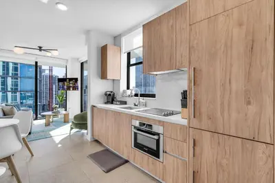 a kitchen with wooden cabinets and a living room at Corner Chic 2 Bedroom Downtown with Rooftop Pool & Views in Miami