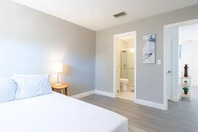 a white bedroom with a bed and a bathroom at Modern 2BR Stay with Desk, Patio, BBQ, Free Parking in Fort Lauderdale