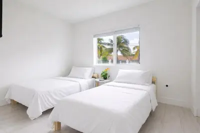 two beds in a white room with a window at Modern 3BR Getaway 4 Beds with Free Parking Included in Hallandale Beach