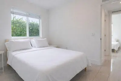 a white bedroom with a white bed and two windows at Modern 3BR Getaway 4 Beds with Free Parking Included in Hallandale Beach