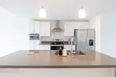 a kitchen with white cabinets and a stainless steel refrigerator at Stylish 3BR Apartment, 4 Beds, Great for Groups with Free Parking in Hallandale Beach