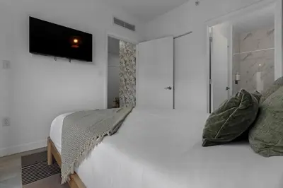 a white bedroom with a bed and a flat screen tv at Voy House Wynwood with Rooftop Pool in Miami