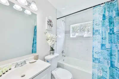 a white bathroom with a blue shower curtain and a toilet at Chill Zona Arizona Villa Perfect Cruise Stay in Fort Lauderdale