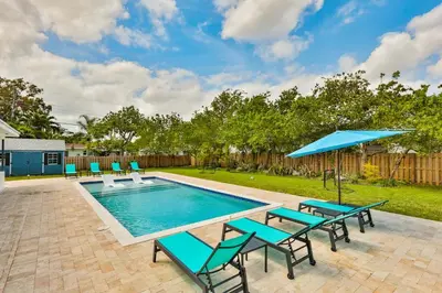 a swimming pool with chairs and a blue umbrella at A star is born villa in Hallandale Beach