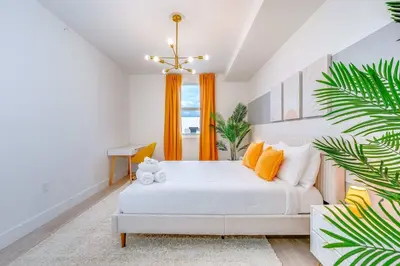 a bedroom with a white bed and orange curtains at Coastal 2BR-2BA Oasis Beach Pool Parking EV Estation in Hallandale Beach