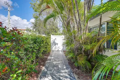 a garden path with a white door and palm trees at Walkable 1BR Apt near Las Olas - Fast WiFi & AC in Fort Lauderdale