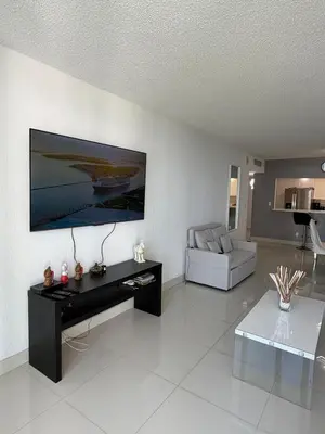 a living room with a table and a tv on a wall at Exceptional apartment in Sunny Isles in Sunny Isles Beach