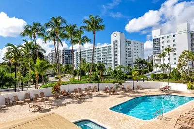 a swimming pool with palm trees and buildings at Le Frontenac 210 STR-01055 in Sunny Isles Beach