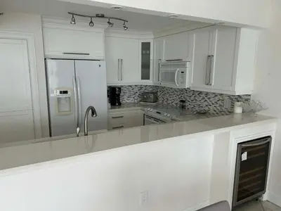 a white kitchen with white cabinets and a refrigerator at Le Laurier in Sunny Isles Beach