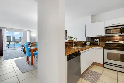 a kitchen with white cabinets and a dining room with a table at Le Marina Bay 1004 STR-02738 in Sunny Isles Beach