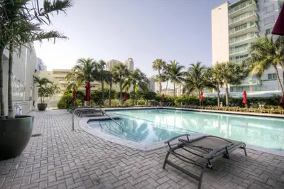 a swimming pool with benches and palm trees in a building at Le Marina Bay 310 STR-01478 in Sunny Isles Beach