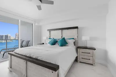 a white bedroom with a large bed with blue pillows at Le Marina Bay PH3 STR-01487 in Sunny Isles Beach