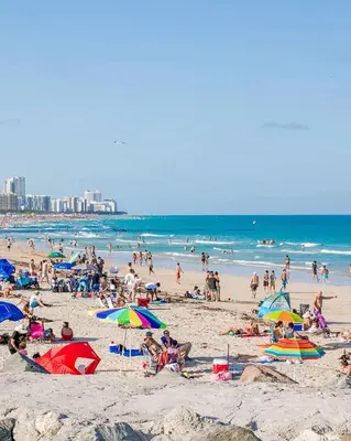 a crowd of people on a beach with umbrellas at Parisian Hotel in Miami Beach