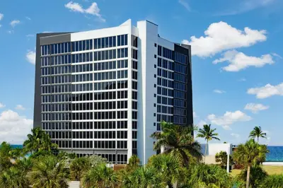 a tall building with palm trees in front of the ocean at Courtyard by Marriott Oceanside Fort Lauderdale Beach in Fort Lauderdale