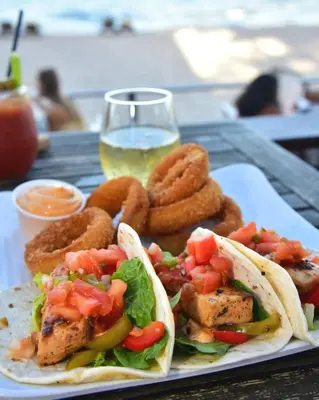 a plate of food with tacos and onion rings and a glass of wine at Sun Tower Hotel & Suites on the Beach in Fort Lauderdale
