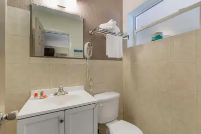 a bathroom with a toilet and a sink and a mirror at Fort Lauderdale Gardens Inn & Suites Ft Lauderdale International Airport in Hollywood