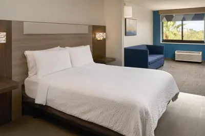 a bedroom with a white bed and a blue chair at Holiday Inn Express Hotel & Suites Kendall East-Miami by IHG in Kendall